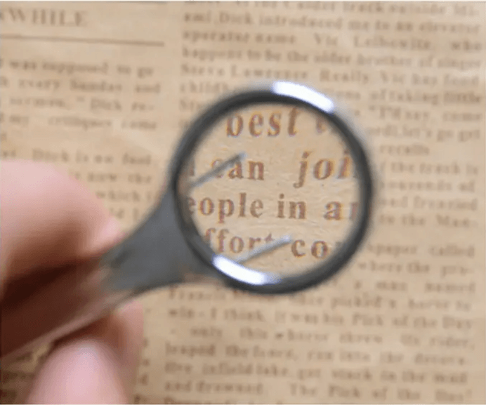 Close-up of a handheld magnifying glass inspecting text on a vintage newspaper.