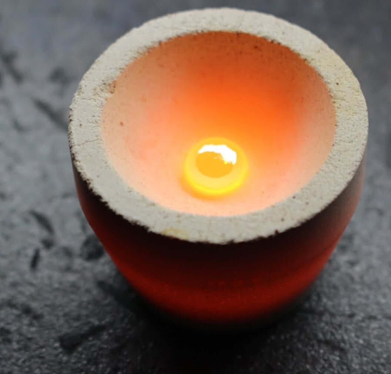 Melting cup with glowing molten material inside, used for precious metal analysis.