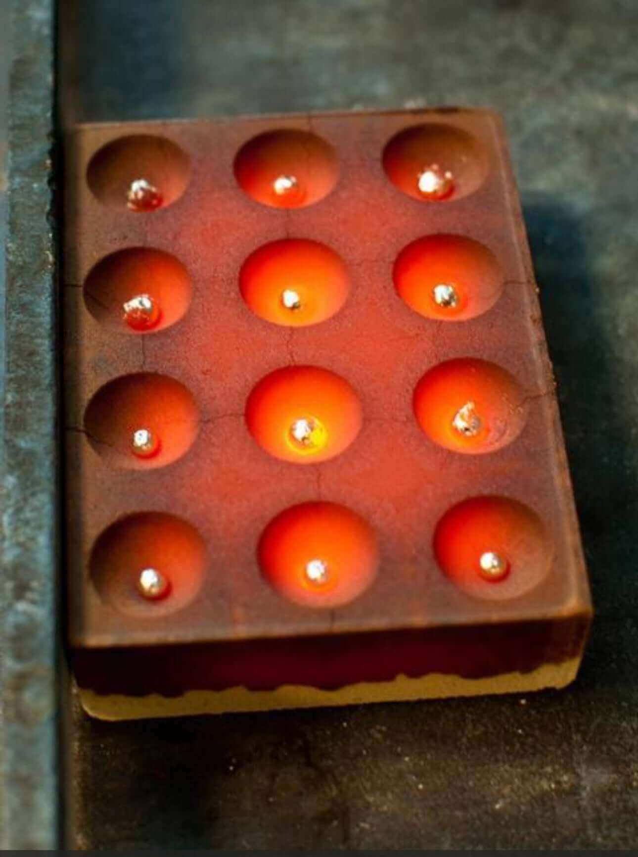 Cupellation lead mold with 12 circular cavities, each with a glowing light, used for precious metal testing.