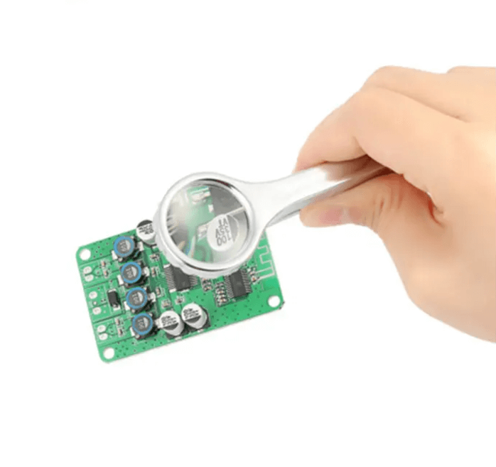 Handheld magnifying glass inspecting a green circuit board, showcasing detail of electronic components.
